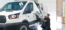 A graphic installer pulling a graphic wrap over a fleet vehicle