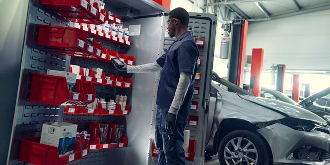 A technician scans inventory inside of a cabinet. A damaged vehicle is shown next to the cabinet.
