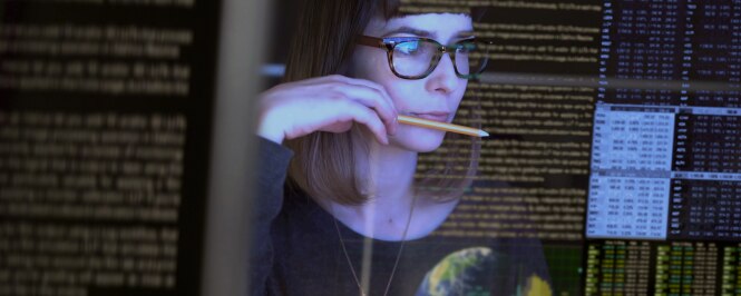 A woman is working in front of multiple computer screens displaying lines of code and data.
