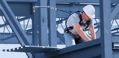Worker kneeling on beam connected to fall protection anchor
