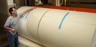 Image of a worker taping down the outer edges of finished paper rolls
