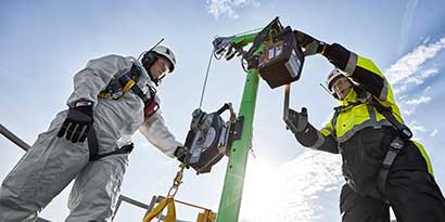 Two industrial workers in protective gear completing setup of confined space entry davit.
