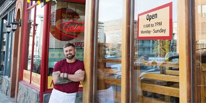 owner standing outside of his restaurant with an 'open' sign on the window. 

