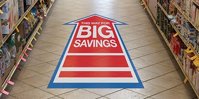 Grocery store aisle floor with arrow-shaped floor graphic reading,” This way for big savings.”
