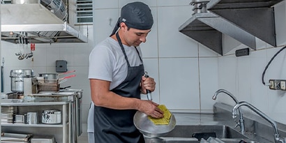 A restaurant worker scrubs a pan in a commercial kitchen.
