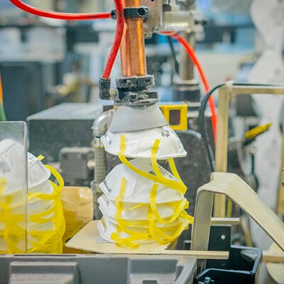 An automated machine picks up a 3M disposable respirator in a factory