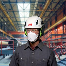 Man wearing safety mask, goggles, helmet and earmuffs.Factory hall in the background.