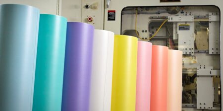 A row of colorful 3M flexographic mounting tape rolls standing vertically in a factory setting.
