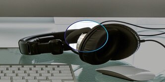 A set of corded foam headphones lay on a glass surface next to a keyboard and mouse. The earmuffs are highlighted where the foam and fabric are bonded.
