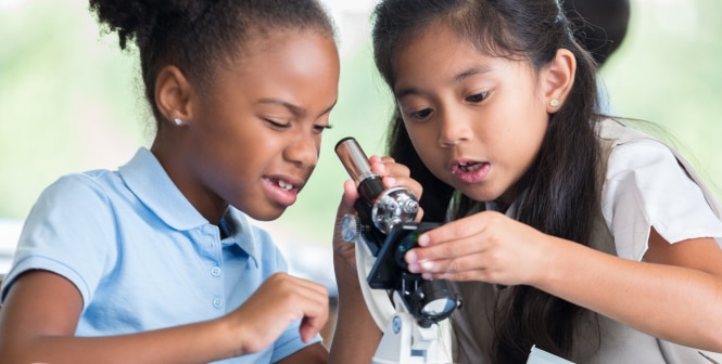 Two students work together using a microscope, with their faces blurred for privacy.
