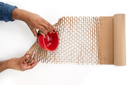 Hands wrapping a red bowl with flexible honeycomb-patterned Scotch&trade; Cushion Lock&trade; Protective Wrap