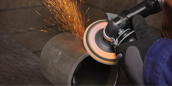 Person deburring a large metal cylinder with a hand held deburrer with sparks being emitted.
