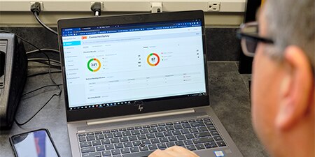 Looking over the shoulder of a man at a laptop with a software dashboard
