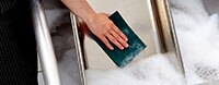 A restaurant worker in a commercial kitchen scours a large pan in soapy water.