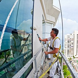 Painter applying paint to a high rise building from a scaffold.