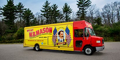 A van with a brightly colored vehicle wrap displays a business name and an image of a man with two American flags.
