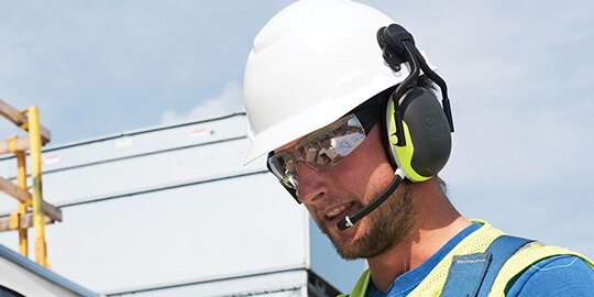 worker outside wearing a hard hat with attached earmuffs hearing protection
