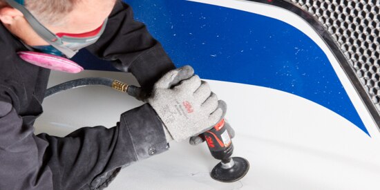 Autobody technician using a small hand held buffer on the hood of a commercial vehicle.
