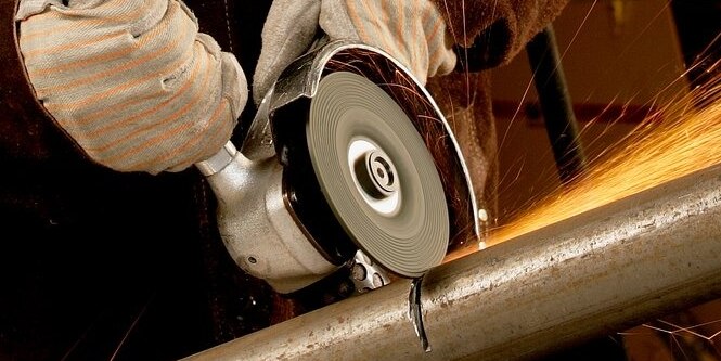  Person cutting metal with a hand held grinder with sparks being emitted.
