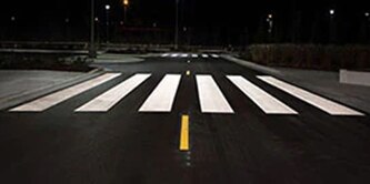 Highly visible pavement markings, including crosswalk and lane dividing line, at night.

