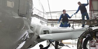 Two people working on an aircraft wing in a hangar.