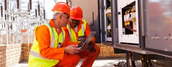 men wearing hard hats working on a laptop at a jobsite.
