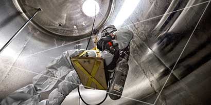 Worker descending into a confined space storage tank wearing protective gear and breathing aparatus.
