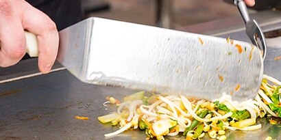 chef cooking onions and peppers on griddle
