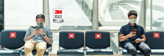 two men wearing masks sitting in chairs looking at their phones - 3M Clean & Protect Certified badge
