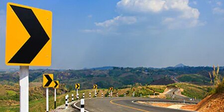 Highly visible road signs indicate a curve in a mountain road.

