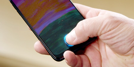 Person holding a phone with their thumb on the front display sensor on the bottom of the screen.
