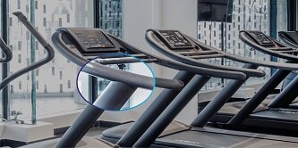 Three treadmills are lined up in a gym setting and the intersection of the handrails and base is highlighted. The highlighted area is enhanced and zoomed in.
