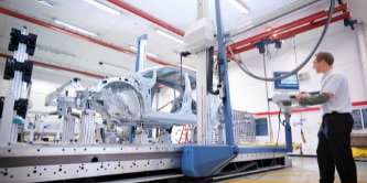 Person working on a machine display in the interior of a factory with machines.
