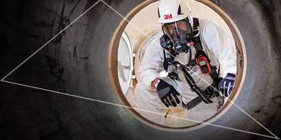 Worker in protective respiratory gear, coveralls and hard hat looking up from confined space
