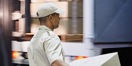 A delivery person bringing a box to a truck
