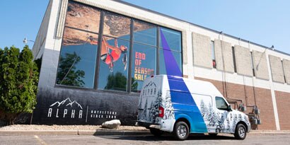 A truck with a vehicle wrap is in front of a building with a large window wrap, and each has strong graphics. 
