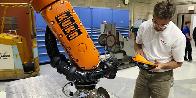 image of an individual standing by a robotic arm
