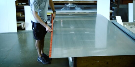 Video screen capture of a man applying 3M™ VHB™ tape to the edges of a large meta sheet for a motorhome laying on a table.
