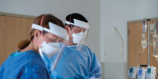 two doctors in patient room wearing respirators
