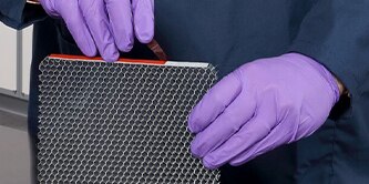 A person with purple gloves holding aerospace bin door materials.