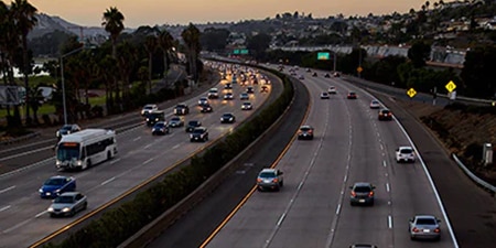 A busy eight-lane highway at dusk has easily viewable pavement markings.
