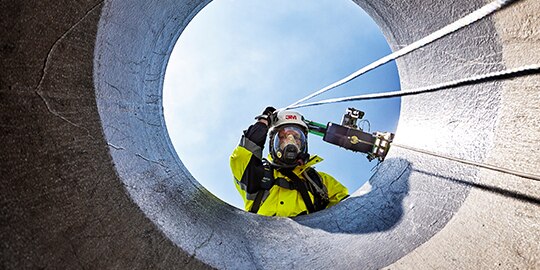 Person wearing 3M Supplied Air System, looking down into a confined space
