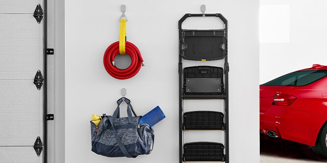 A wall in a garage with 3M CLAW™ Drywall Hooks hanging a hose, step ladder, and a camp chair.
