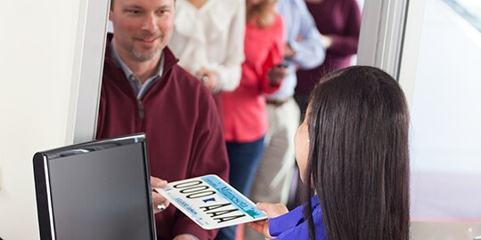 A DMV worker hands a license plate to a customer.
