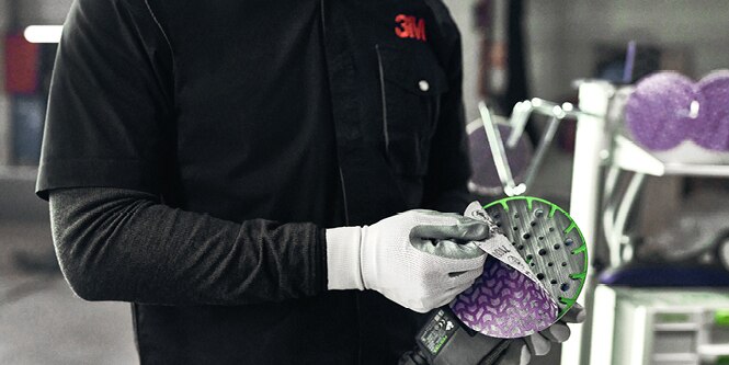 Man peeling 3M Cubitron II abrasive disc off handheld tool
