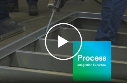 Video still of liquid adhesive application to a frame before adding a panel, with text &ldquo;Process &ndash; Integration Expertise&rdquo;