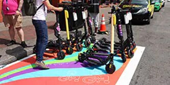 Colorful painted pavement for scooter parking on urban road, with scooters and person holding handlebars of scooter.
