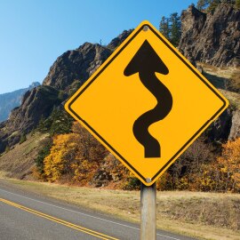 Alt Text: Yellow diamond-shaped road sign warning of a winding road ahead.