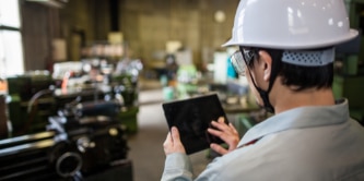 Person in a white hard hat holding a tablet and touching the screen.
