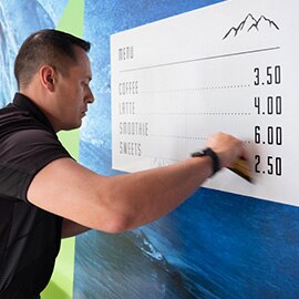 Man installing printed graphic film featuring wave image mural and cafe menu to wall